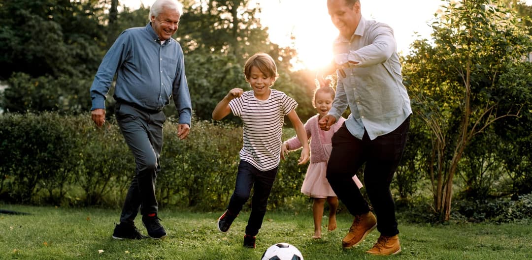 Bestefar, far og barn spiller fotball på plenen